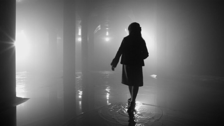 A silhouetted figure walking through a wet interior.